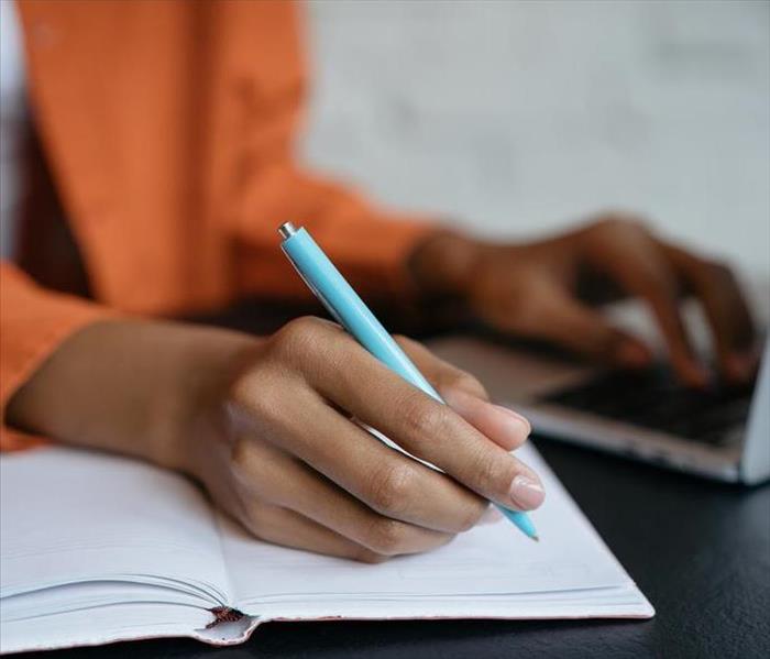 A woman writing in a notebook with a computer.
