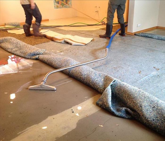 Carpet pulled back with water underneath and a vacuum extracting water